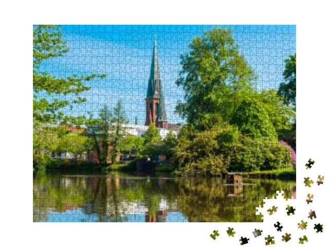 Puzzle 1000 Teile „Blick auf den Teich und die St. Lamberti Kirche in Oldenburg, Deutschland“