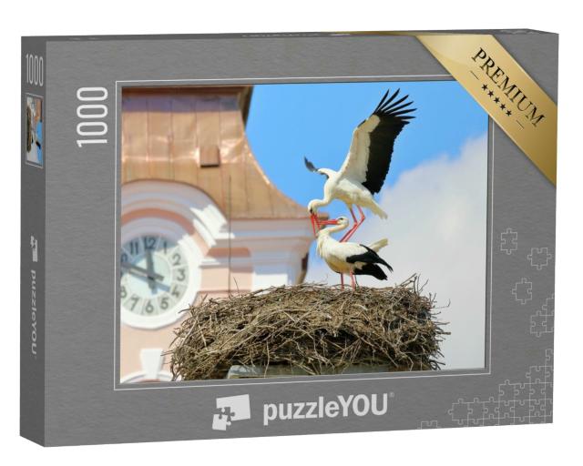 Puzzle 1000 Teile „Paarung von Weißstörchen im Nest auf einer Kirche“